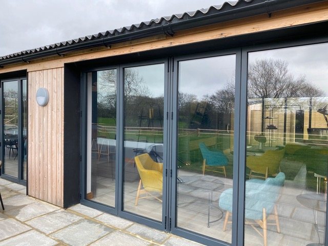 A finished single-storey building clad in vertical timber with dark grey bi-fold doors