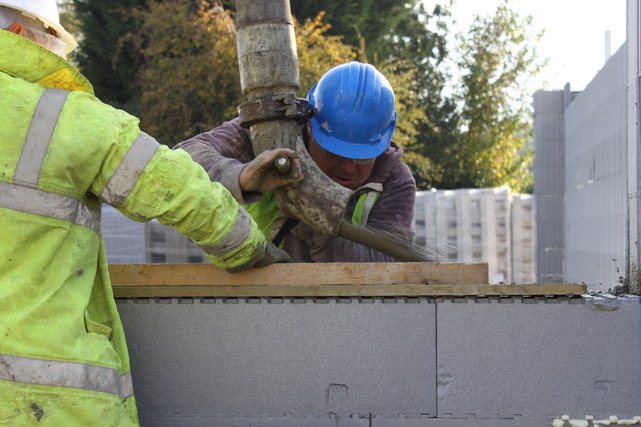A worker steadying the concrete pump hose over the open top of a wall