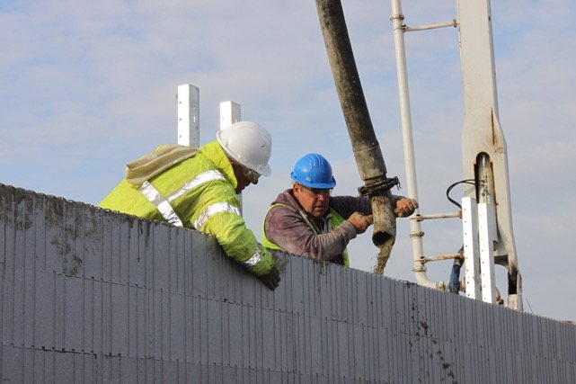 Two workers directing a concrete pump hose along the top of a formwork wall